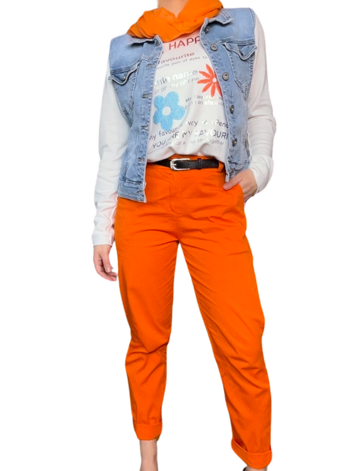 Pantalon cigarette orange pour femme avec ceinture noire, chandail blanc à manche longue, foulard orange et veste en jeans.