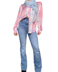 Jeans pour femme flare clair à taille haute avec blouse à carreaux abstraits, foulard bleu ciel et et bottes noires.