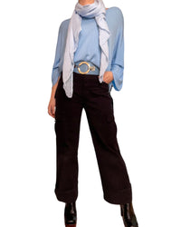 Chandail bleu pâle femme à manche longue col en v avec foulard blanc, ceinture bleue, jeans cargo noir et bottes noires.