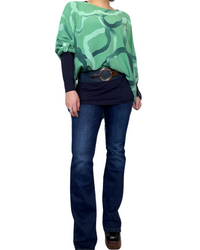 Blouse verte oversize pour femme à motifs avec chandail à manche longue, ceinture, jeans flare et bottes noires.