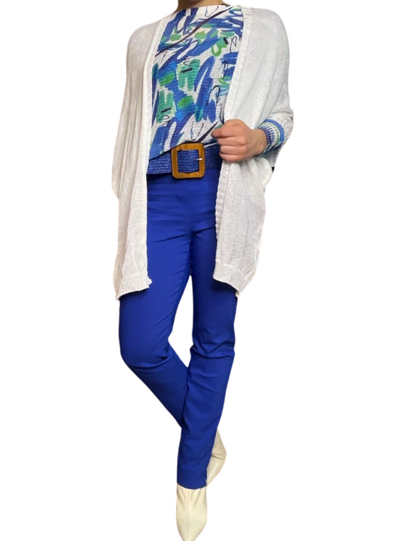 Chandail blanc pour femme à manche longue avec imprimé bleu et vert avec veste en tricot, ceinture, pantalon bleu et bottes beige.