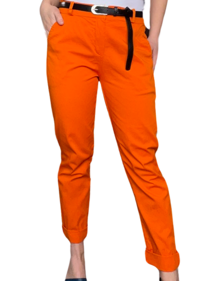 Pantalon cigarette orange pour femme avec ceinture noire et camisole gainante blanche.