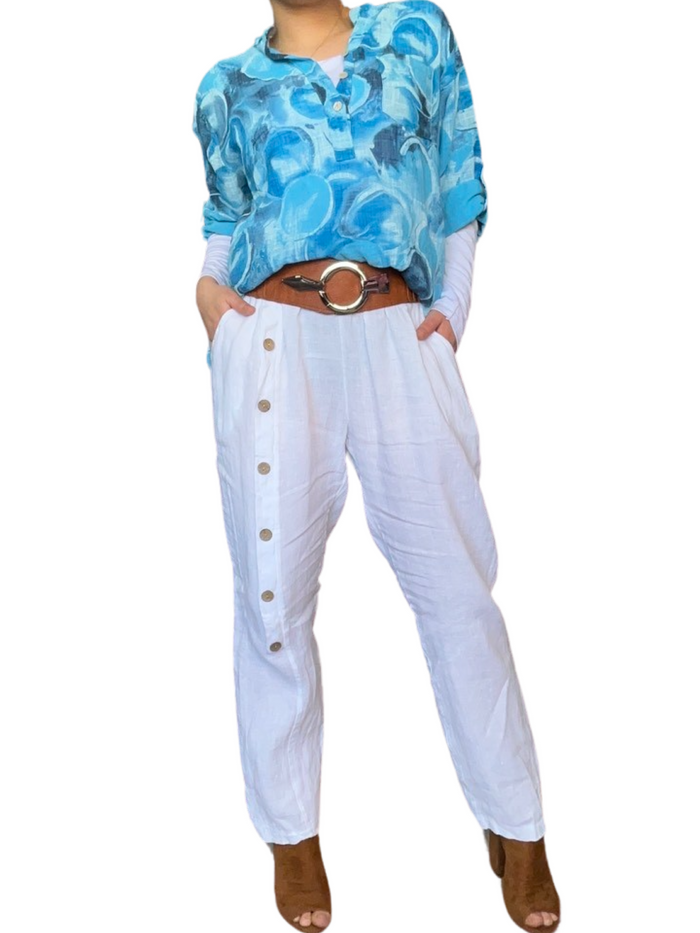 Blouse turquoise pour femme avec imprimé de ronds abstraits avec ceinture camel et pantalon en lin blanc.