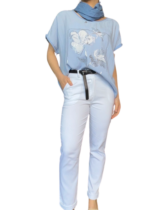 T-shirt bleu clair pour femme avec imprimé d'une fleur avec pantalon blanc et ceinture noire.
